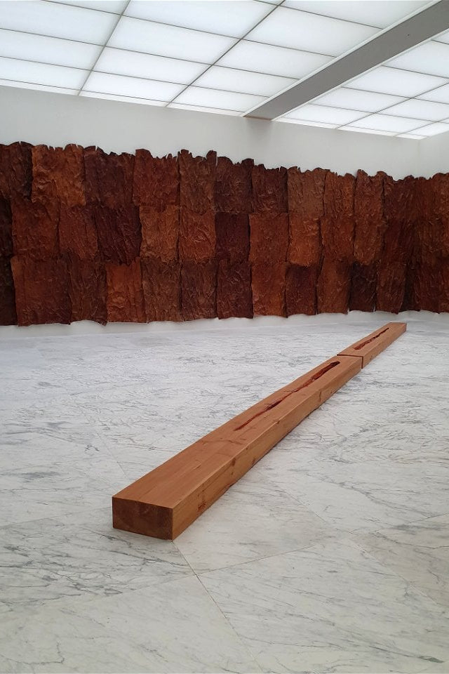 Long wooden block on a marble floor with textured wall in the background Giuseppe Penone